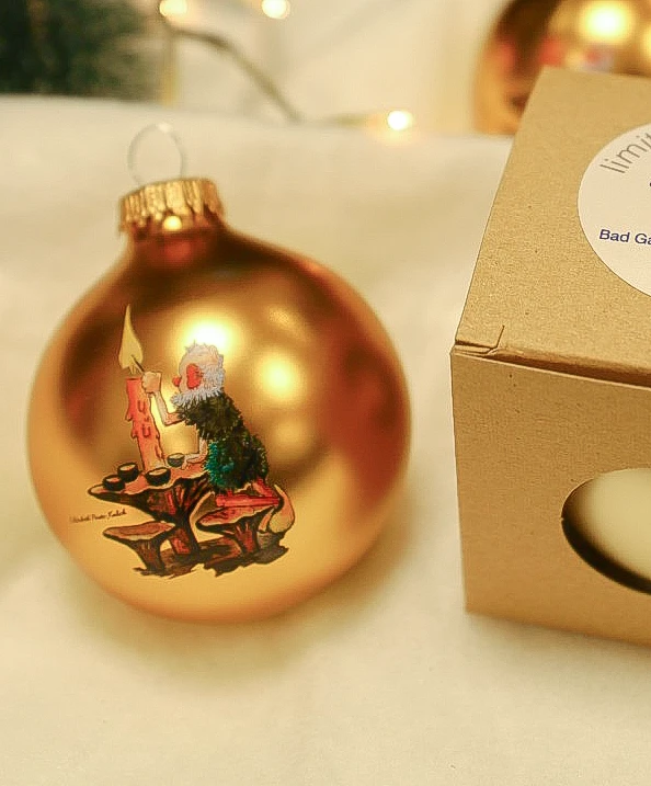 Das farbige Mooswicht-Motiv auf der goldenen Weihnachtskugel 2025